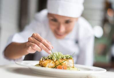 A professional chef meticulously plating a fine dining fish dish on a white plate