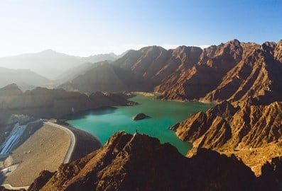 Aerial view of the Hatta Dam site framed by sun-lit mountains.
