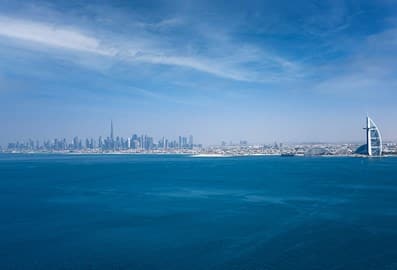 Panoramic view of Dubai's sunny skyline in front of the clear blue sea.