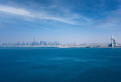 Panoramic view of Dubai's sunny skyline in front of the clear blue sea.