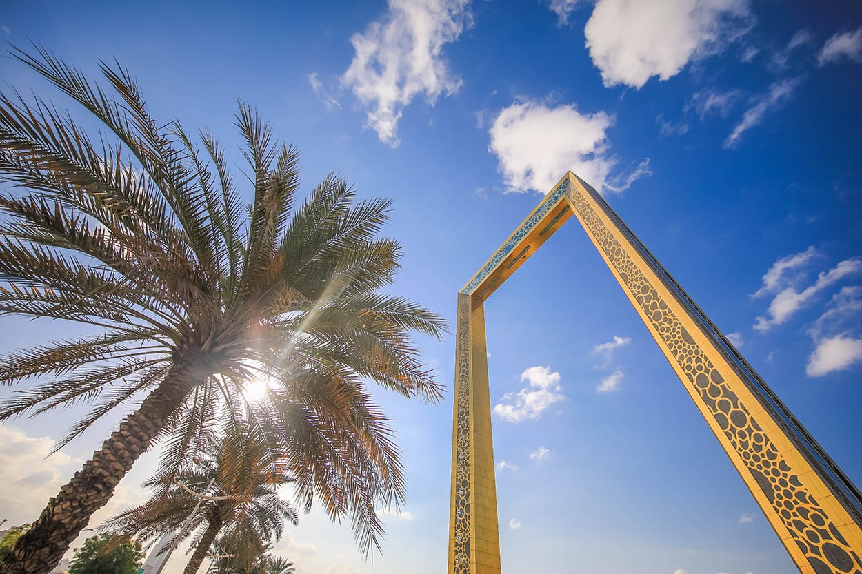 The golden Dubai Frame rising against a bright blue sky beside palm fronds