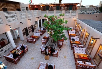 Traditional courtyard seating with wooden benches and a central tree at Al Khayma