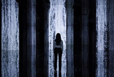 Woman standing in an immersive experience facing columns with waterfall projection