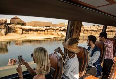 Visitors on a bus passing by a water channel with hippos while taking photographs.