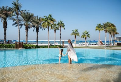 Woman holding a girl's hand beside a swimming pool at Four Seasons Resort Dubai at Jumeirah Beach