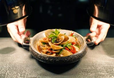 Stir-fried clams in a rustic stone bowl at Hawkerboi restaurant