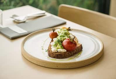Avocado and cream cheese toast with vine-ripened cherry tomatoes on a ceramic plate at Teible restaurant