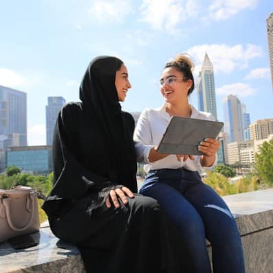 Two students talking outdoors with Dubai buildings behind them