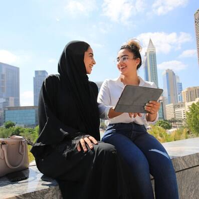 Two students talking outdoors with Dubai buildings behind them