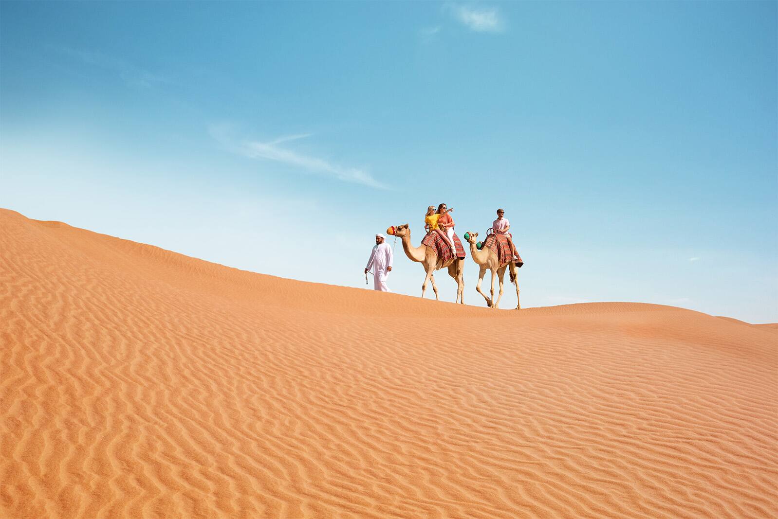 A small group of tourists on camels riding through the desert dunes.