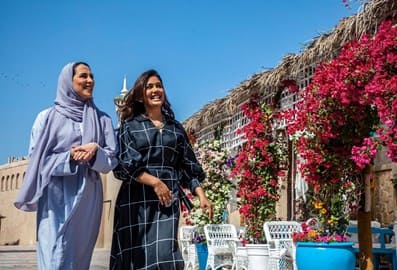 Two women walking outdoors next to flowers in old Dubai.