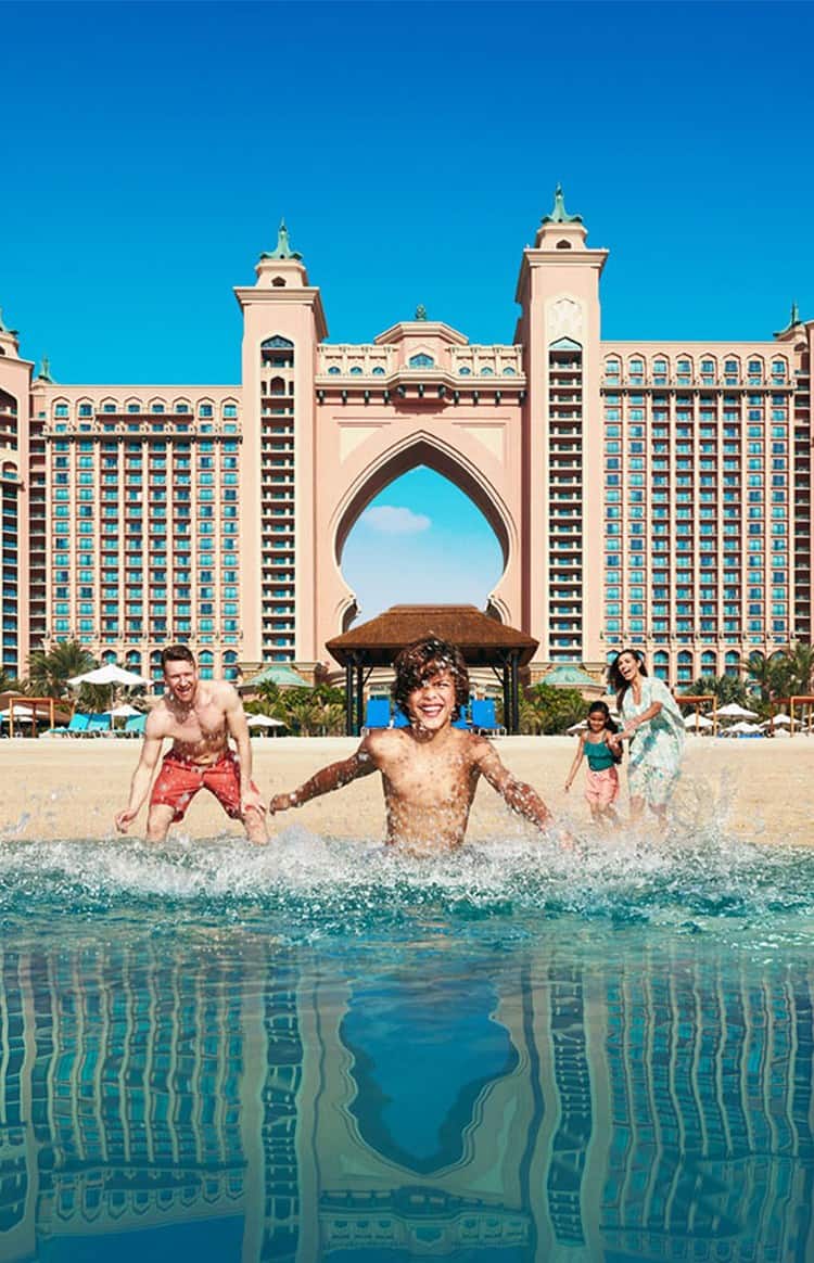 A young family running into the sea with Atlantis, The Palm in the background.