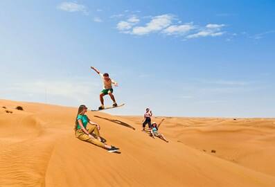Group sandboarding on the dunes in the Dubai desert.