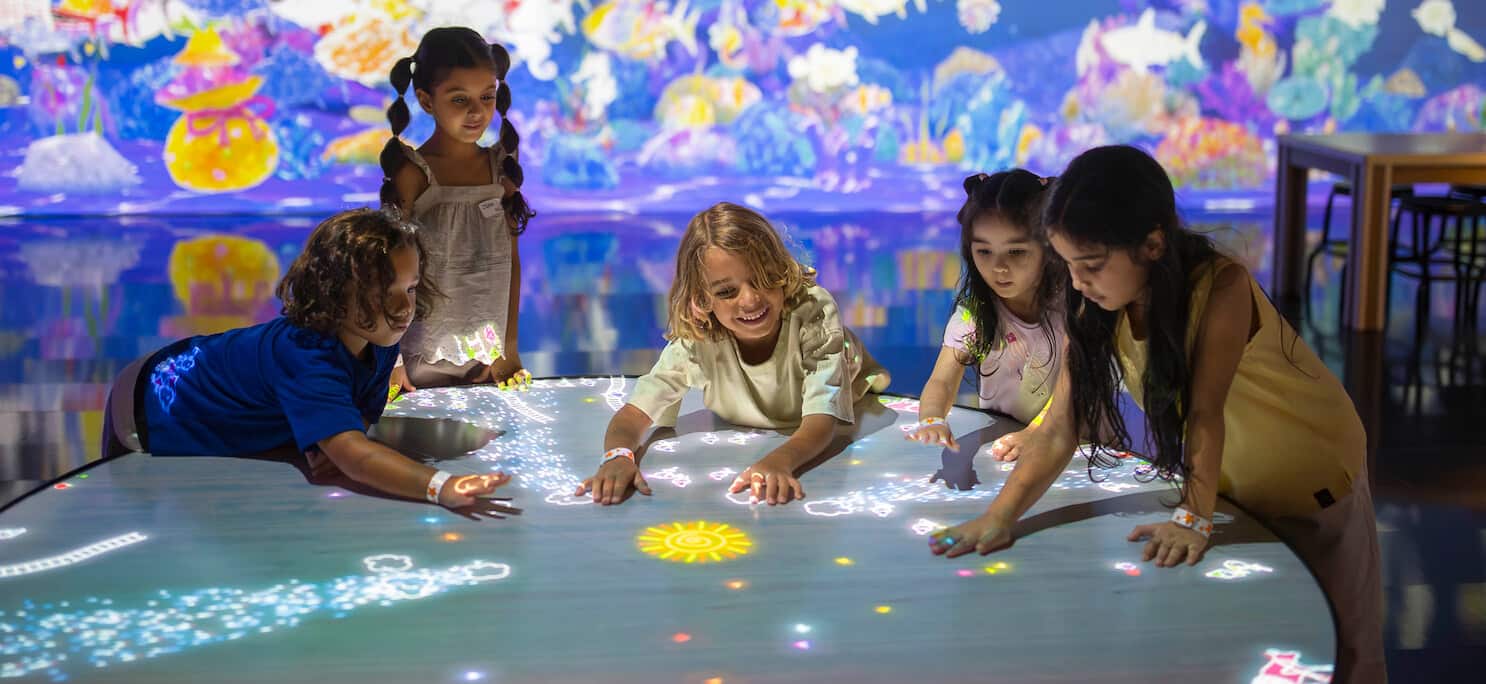 OliOli - children sitting around an illuminated table looking at light figures.