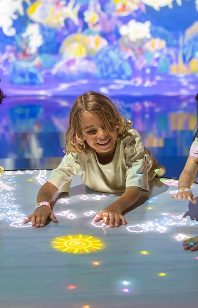 OliOli - children sitting around an illuminated table looking at light figures.