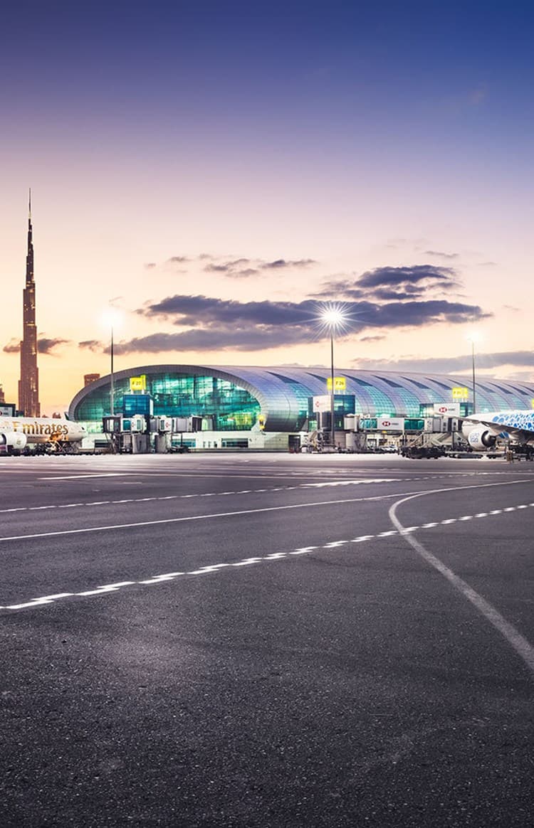 Panoramic view of the outdoor area of Dubai International Airport with parked Emirates planes in front of the building.