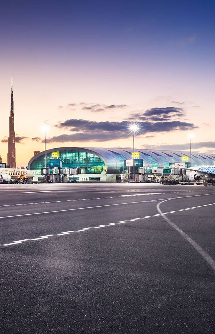 Panoramic view of the outdoor area of Dubai International Airport with parked Emirates planes in front of the building.