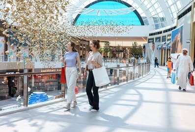 Two women walk together carrying shopping bags through a bright, modern indoor mall walkway
