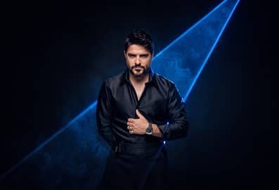 An artist in a black shirt poses dramatically against a smoky, blue-lit backdrop