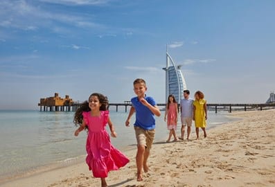 Family running on a beach in front of Burj Al Arab